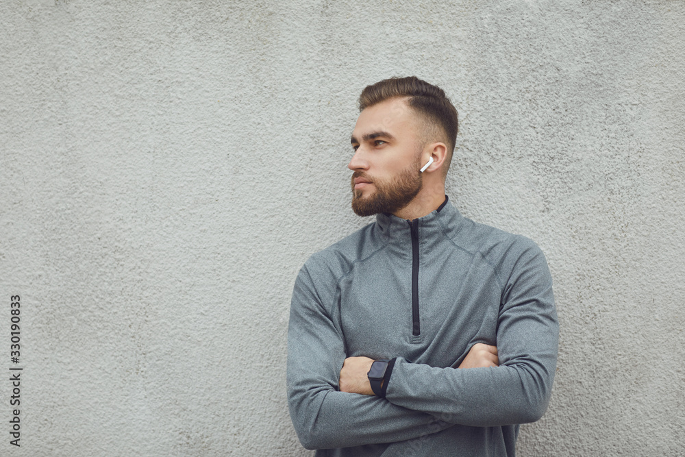 Bearded guy in gray sportswear with headphones on a gray background. Bearded guy in gray sportswear with headphones on a gray background.