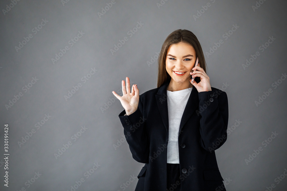 Young pretty girl in business style clothes stands on a gray background with a mobile phone in her hands. Business style Young pretty girl in business style clothes stands on a gray background with a mobile phone in her hands. Business style