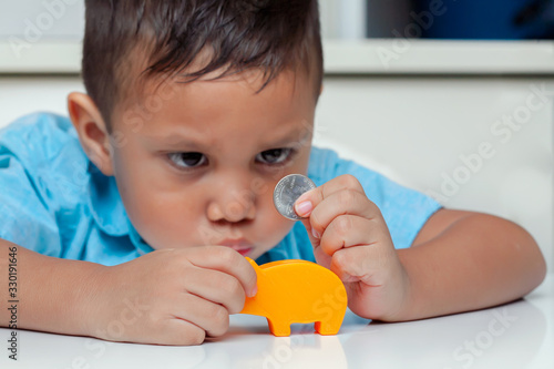 A 4 year old boy starring at a U.S. coin that he is about to put into a small savings piggy bank.