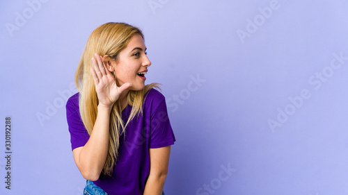 Young blonde woman isolated on purple background trying to listening a gossip.