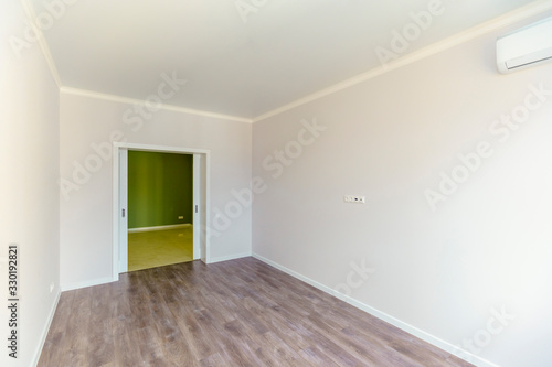 An empty room with white walls and wooden floors . Fresh new renovation. The door to the corridor.