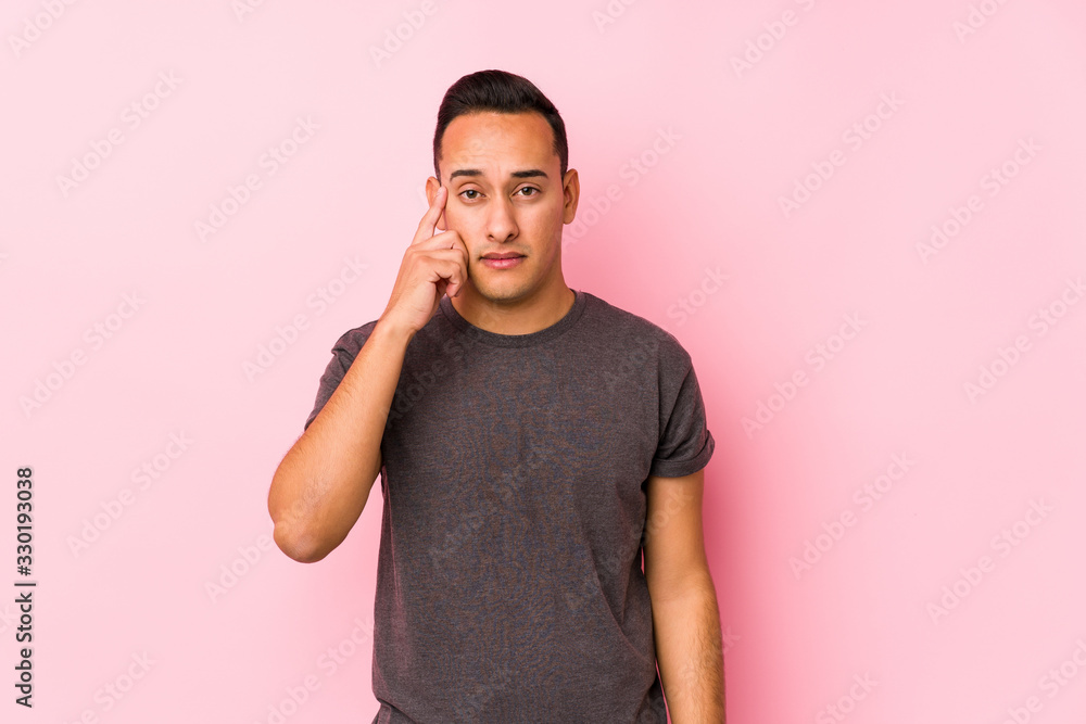 Yooung latin man posing in a pink backgroundpointing temple with finger, thinking, focused on a task. Yooung latin man posing in a pink backgroundpointing temple with finger, thinking, focused on a task.