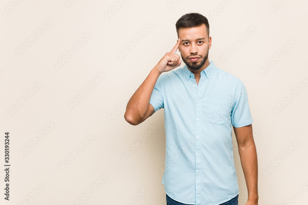 Young south-asian man pointing temple with finger, thinking, focused on a task. Young south-asian man pointing temple with finger, thinking, focused on a task.