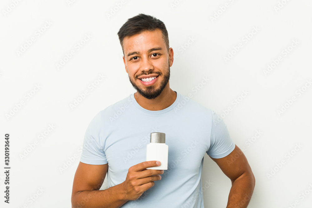 Young south-asian man holding an after shave cream happy, smiling and cheerful. Young south-asian man holding an after shave cream happy, smiling and cheerful.
