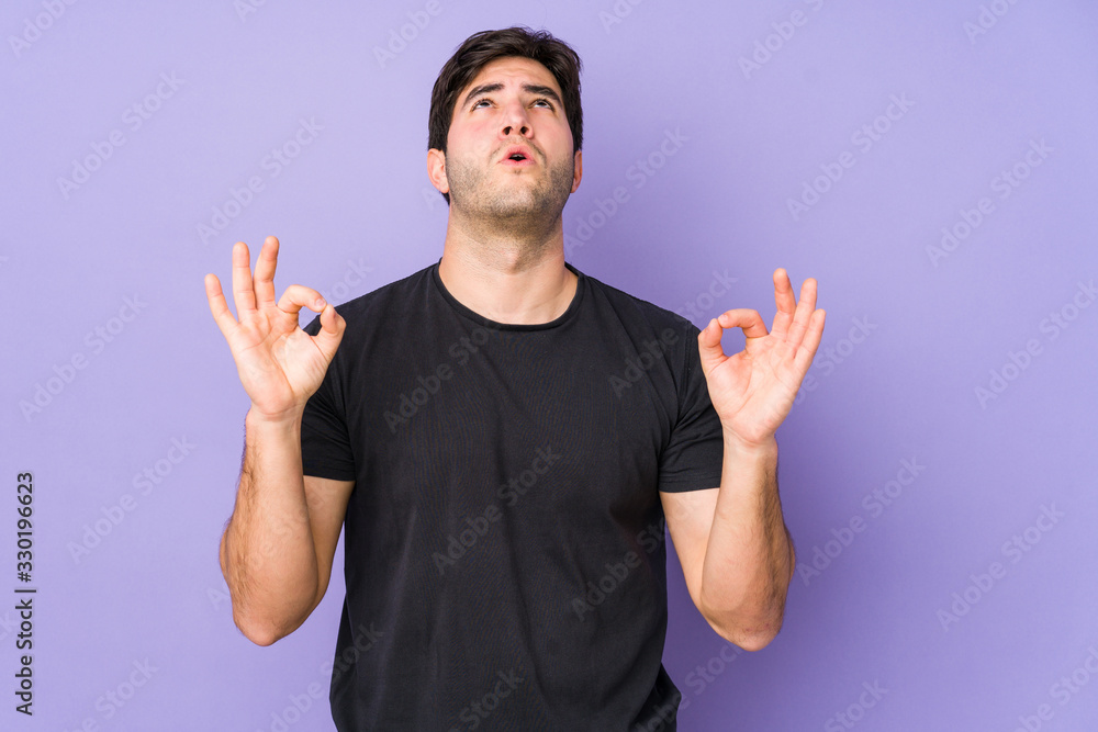 Fototapeta premium Young man isolated on purple background relaxes after hard working day, she is performing yoga.