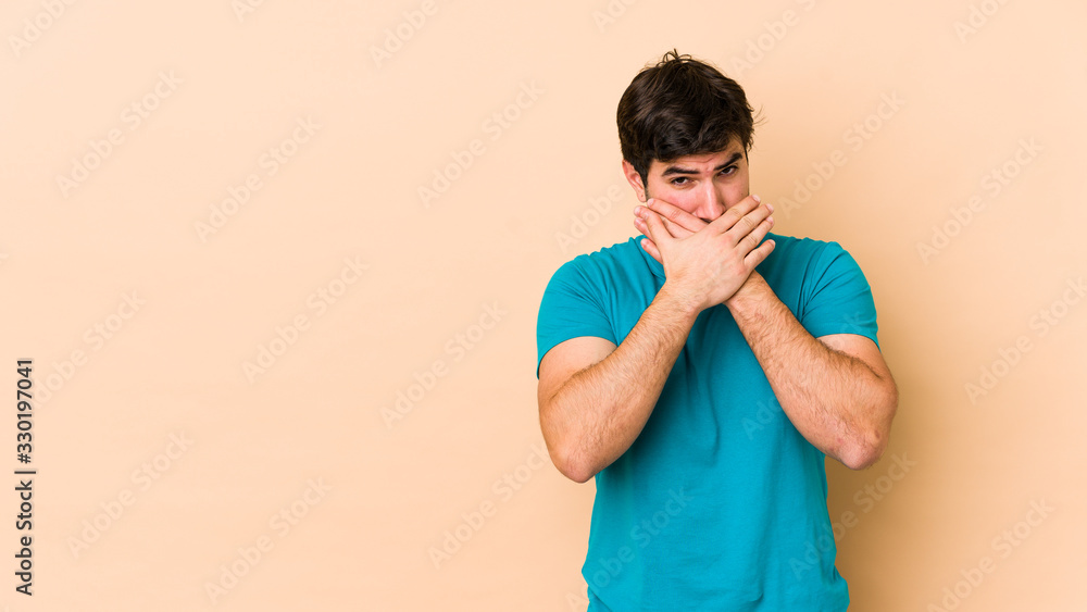 Young man isolated on beige background covering mouth with hands looking worried. Young man isolated on beige background covering mouth with hands looking worried.