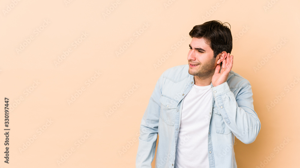 Young man isolated on beige background trying to listening a gossip. Young man isolated on beige background trying to listening a gossip.