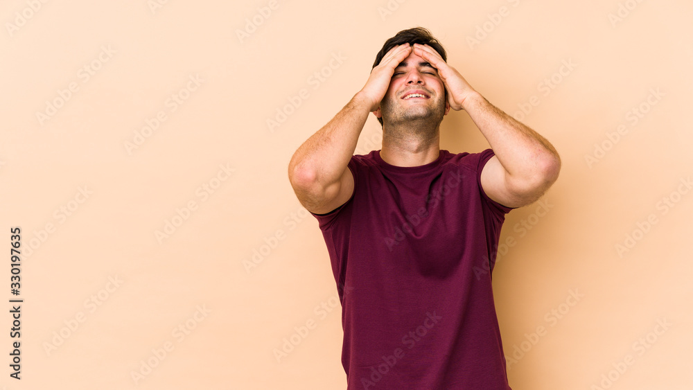 Young man isolated on beige background laughs joyfully keeping hands on head. Happiness concept. Young man isolated on beige background laughs joyfully keeping hands on head. Happiness concept.