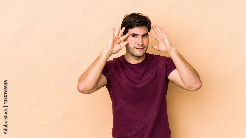 Young man isolated on beige background receiving a pleasant surprise, excited and raising hands. Young man isolated on beige background receiving a pleasant surprise, excited and raising hands.