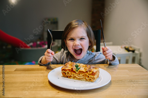 Little girl with a lasagne bolognese in a cafe