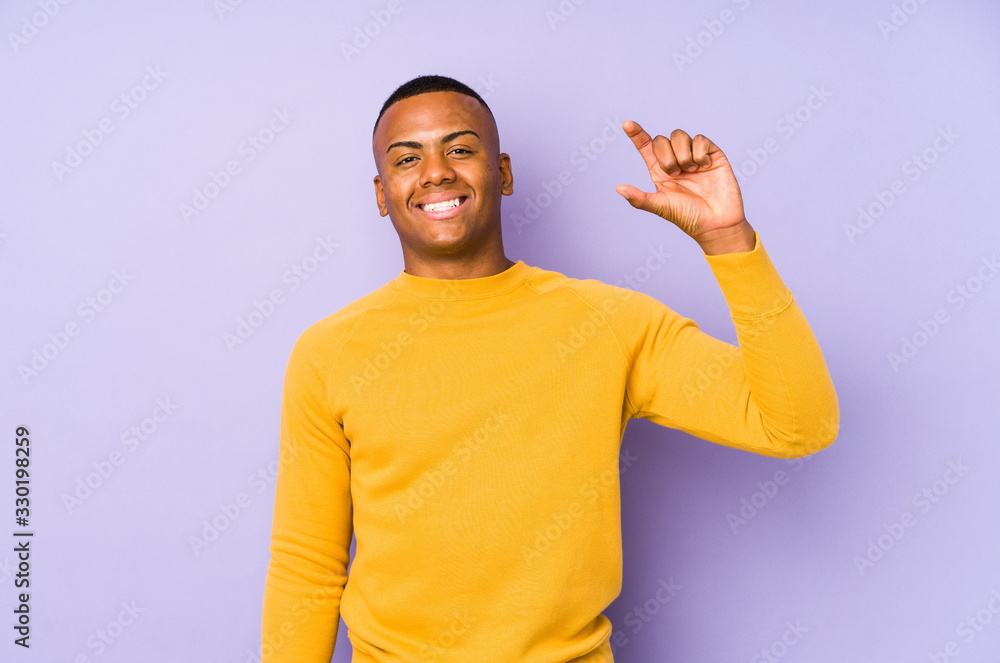 Naklejka premium Young latin man isolated on purple background holding something little with forefingers, smiling and confident.