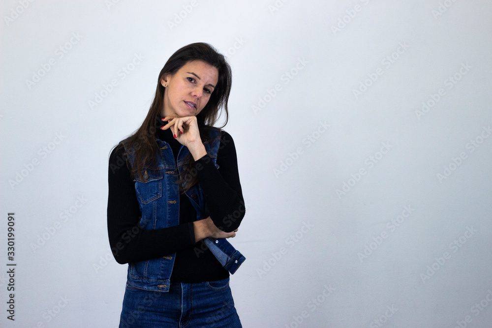 Portrait of caucasian middle age woman looking seriouss and pensive directly at camera, isolated on gray background studio shot, black sweater, denim jacket, jeans, dark air. Place for your text in co Portrait of caucasian middle age woman looking seriouss and pensive directly at camera, isolated on gray background studio shot, black sweater, denim jacket, jeans, dark air. Place for your text in co