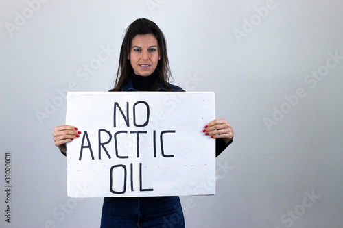 attractive  middle age woman activist hold up protesting sign saying "No arctic oil" isolated on gray background studio shot, dark air. Place for your text in copy space.