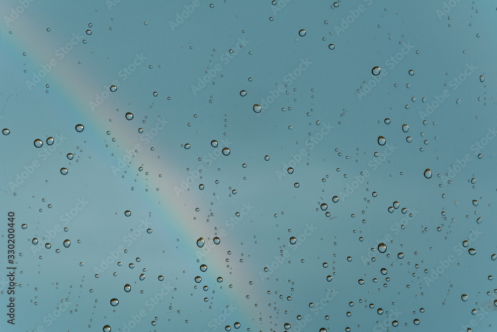 A rainbow behind a glass windows with water drops. A rainbow behind a glass windows with water drops.