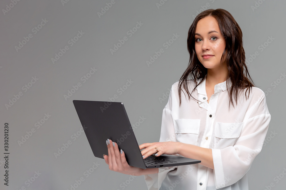Charming young woman working freelance, remote from office, hold laptop, typing university essay, turn left smiling copy space, stand gray background joyful, browsing web using computer Charming young woman working freelance, remote from office, hold laptop, typing university essay, turn left smiling copy space, stand gray background joyful, browsing web using computer