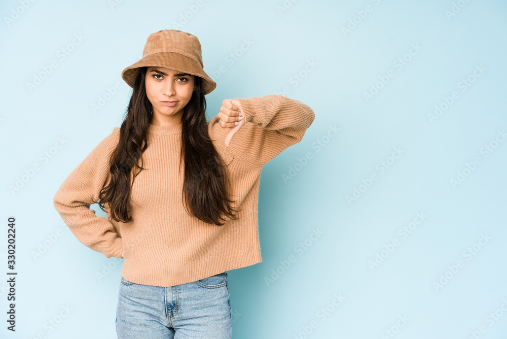 Young indian woman wearing a hat isolated on blue background showing thumb down, disappointment concept. Young indian woman wearing a hat isolated on blue background showing thumb down, disappointment concept.