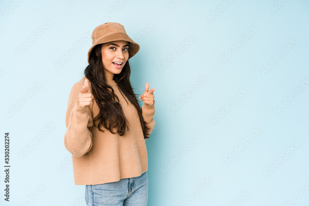 Young indian woman wearing a hat isolated on blue background pointing to front with fingers. Young indian woman wearing a hat isolated on blue background pointing to front with fingers.