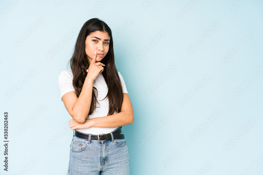 Young indian woman on blue background contemplating, planning a strategy, thinking about the way of a business. Young indian woman on blue background contemplating, planning a strategy, thinking about the way of a business.
