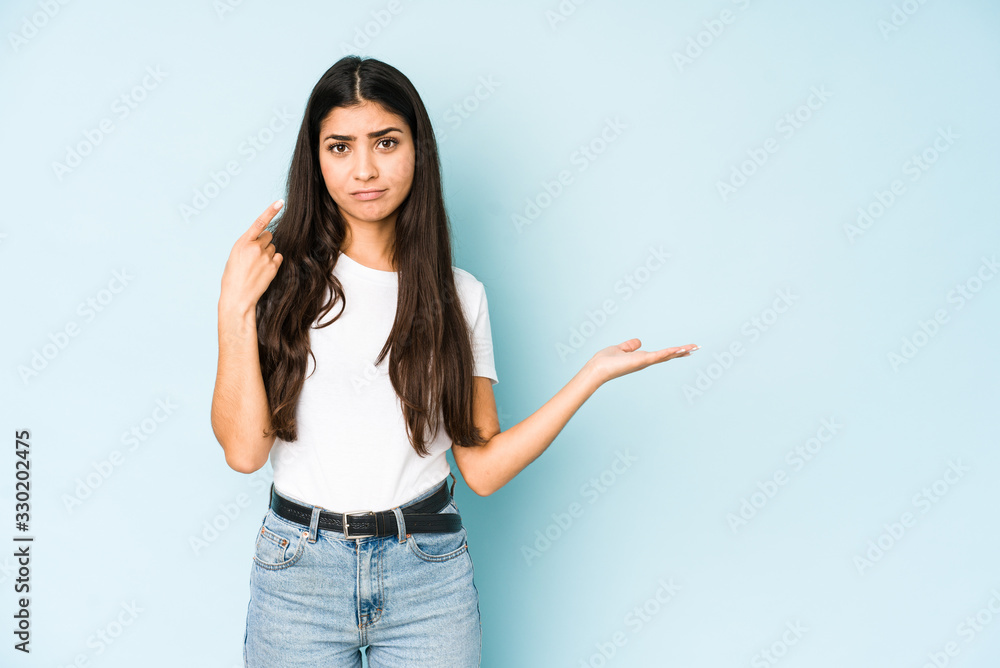 Young indian woman on blue background holding and showing a product on hand. Young indian woman on blue background holding and showing a product on hand.