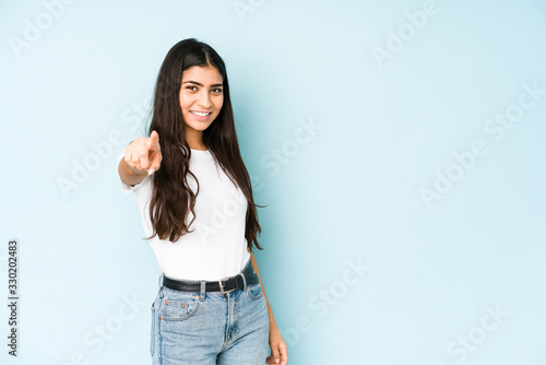 Young indian woman on blue background pointing to front with fingers.