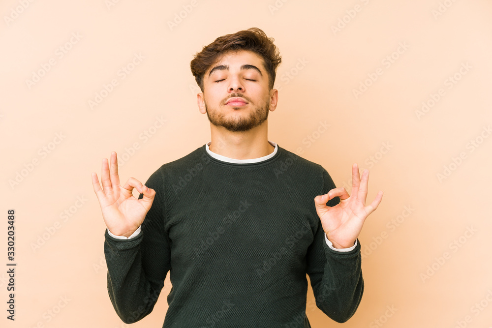 Young arabian man isolated on a beige background relaxes after hard working day, she is performing yoga. Young arabian man isolated on a beige background relaxes after hard working day, she is performing yoga.