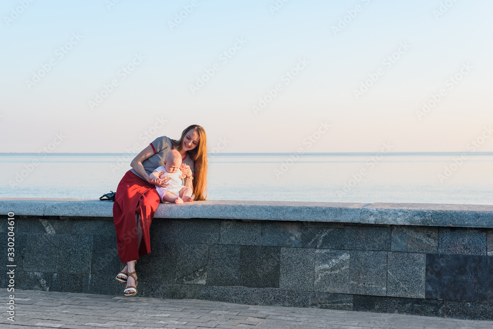 Young mother and baby to sit on promenade and sea. Vacation with baby at sea