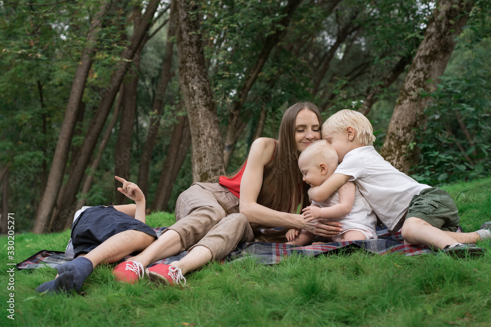 Family picnic at gaden park outdoors. Mom and three children rest on picnic blanket. Family picnic at gaden park outdoors. Mom and three children rest on picnic blanket.