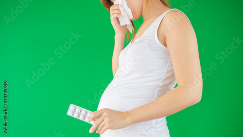 Pregnant woman is coughing and feeling sick from allergy, virus or respiratory disease. Pregnant woman on isolated green background.