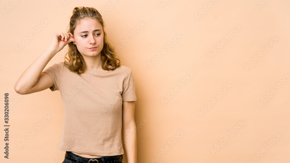 Young caucasian woman isolated on beige background covering ears with fingers, stressed and desperate by a loudly ambient. Young caucasian woman isolated on beige background covering ears with fingers, stressed and desperate by a loudly ambient.