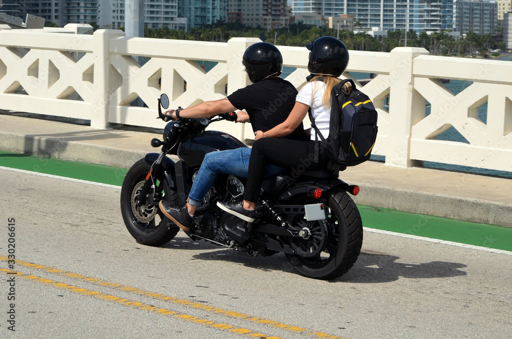 Young couple riding tandem on aa motorcycle waiting for the Venetia Causeway bridge in Maimi Beach Florida to open to traffic