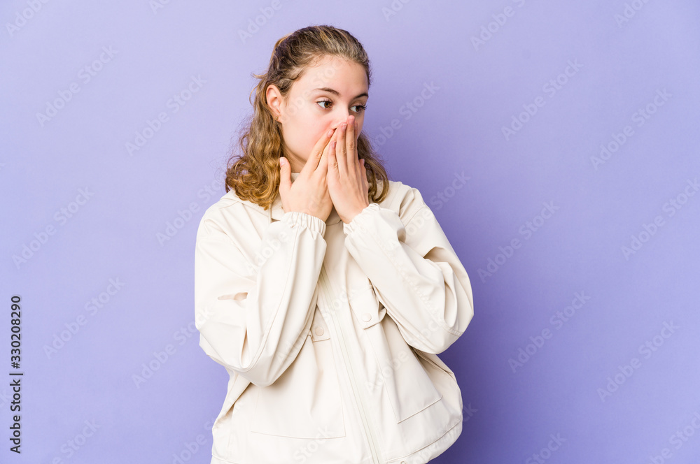 Young caucasian woman on purple background thoughtful looking to a copy space covering mouth with hand. Young caucasian woman on purple background thoughtful looking to a copy space covering mouth with hand.