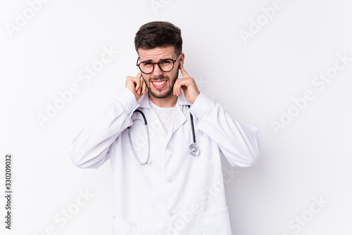 Young caucasian doctor man isolated covering ears with hands.