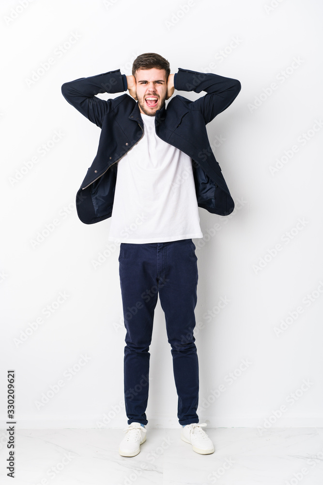 Full body young caucasian man isolated covering ears with hands trying not to hear too loud sound. Full body young caucasian man isolated covering ears with hands trying not to hear too loud sound.
