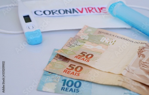 Brazilian Real banknotes with face mask, syringe and thermometer in the background. Coronavirus Alert. Economy concept. 