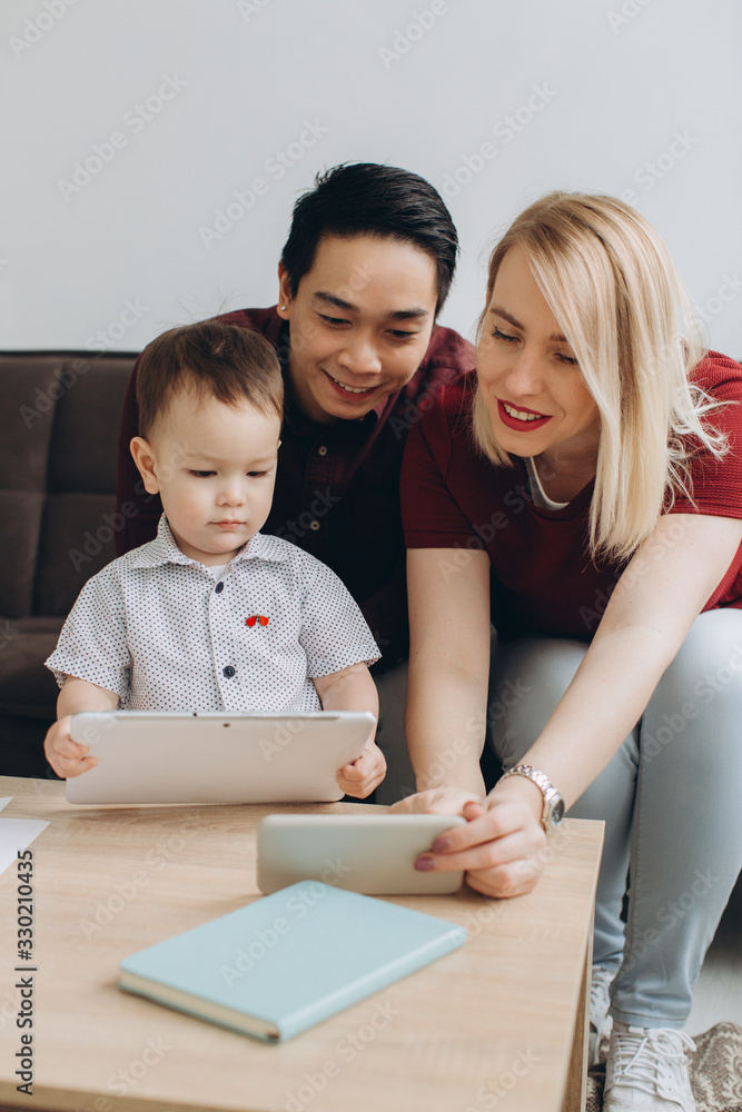 Happy multicultural family. Asian man and Caucasian woman with their son watching video on tablet and smartphone. Happy multicultural family. Asian man and Caucasian woman with their son watching video on tablet and smartphone.
