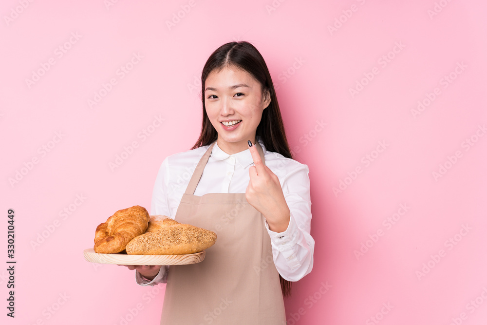 Young chinese baker woman isolated pointing with finger at you as if inviting come closer. Young chinese baker woman isolated pointing with finger at you as if inviting come closer.