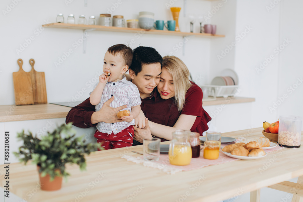 Happy multicultural family. Asian dad and his caucasian blonde wife have breakfast with their beautiful son in the kitchen. Happy multicultural family. Asian dad and his caucasian blonde wife have breakfast with their beautiful son in the kitchen.