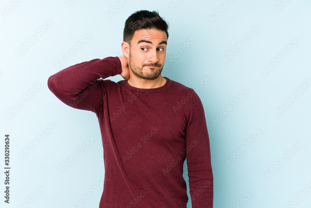 Young caucasian man isolated on blue background touching back of head, thinking and making a choice. Young caucasian man isolated on blue background touching back of head, thinking and making a choice.