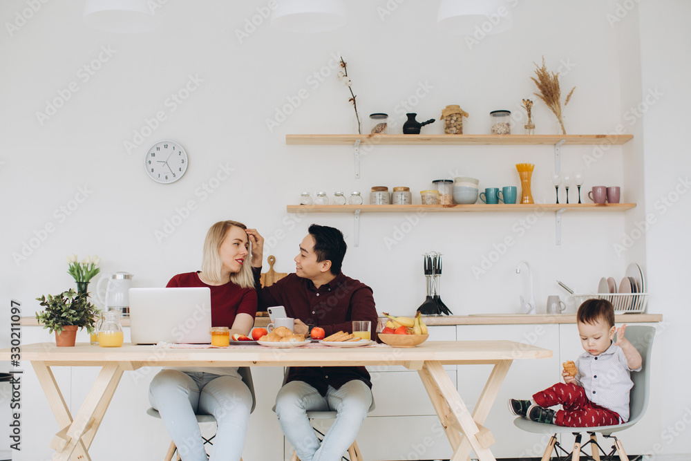 Asian dad and european mom work with their gadgets, and son has breakfast alone. Modern technological problems.