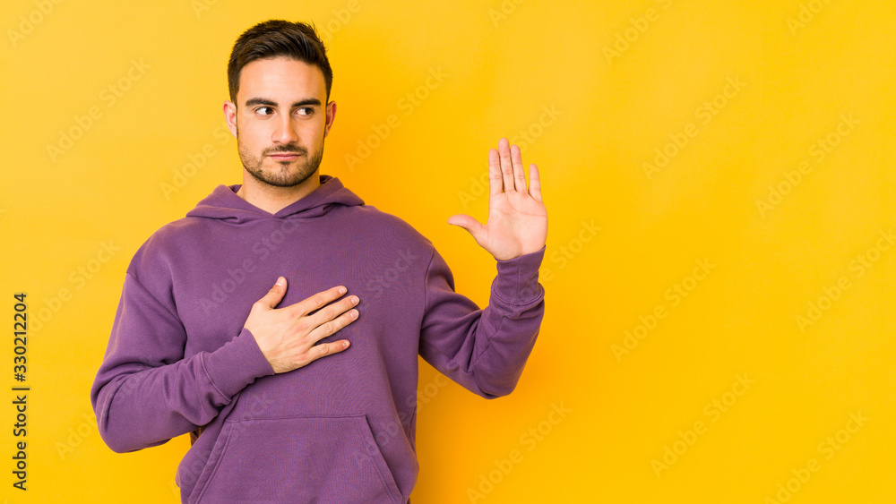 Young caucasian man isolated on yellow bakground taking an oath, putting hand on chest. Young caucasian man isolated on yellow bakground taking an oath, putting hand on chest.