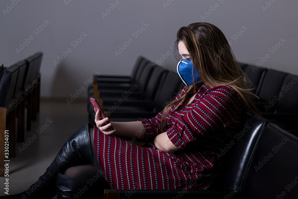 Obraz premium Busy woman with mobile phone and protective mask sitting alone in conference room. Corona concept
