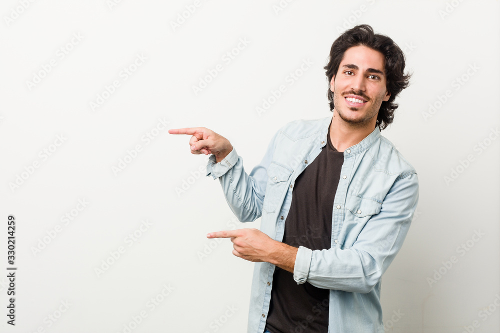 Young handsome man against a white background excited pointing with forefingers away. Young handsome man against a white background excited pointing with forefingers away.