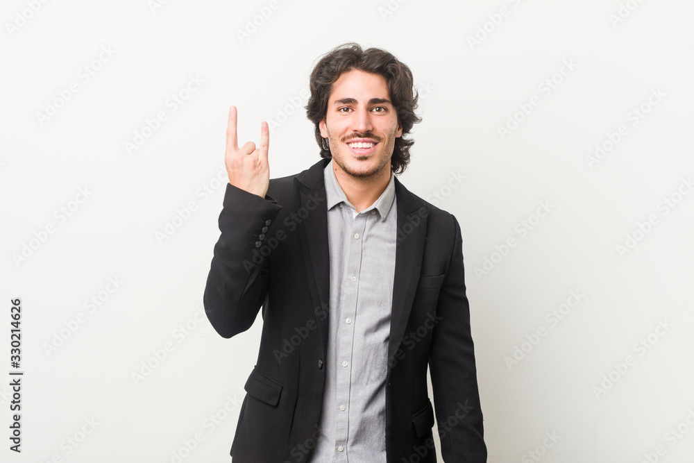 Young business man against a white background showing a horns gesture as a revolution concept. Young business man against a white background showing a horns gesture as a revolution concept.