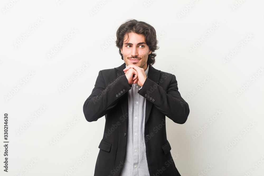 Young business man against a white background keeps hands under chin, is looking happily aside. Young business man against a white background keeps hands under chin, is looking happily aside.