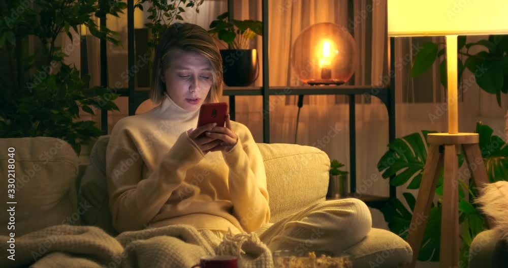 Thoughtful woman text messaging using mobile phone sitting on sofa at night Thoughtful woman text messaging using mobile phone sitting on sofa at night