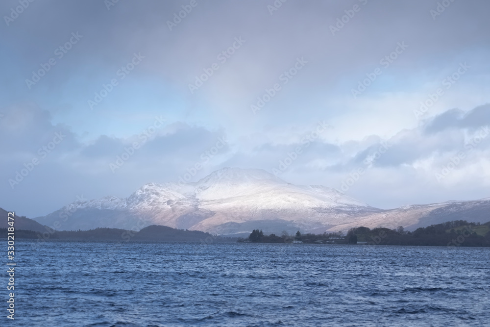 Calm peaceful atmospheric view of lake at Loch Lomond during change of weather from rain to sunshine in winter