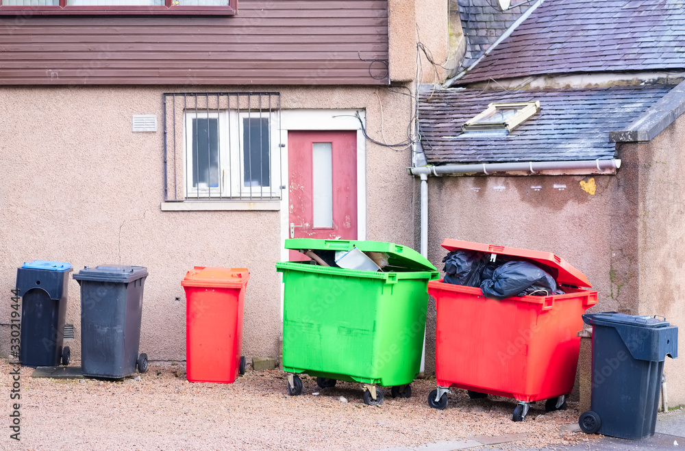 Wheelie bin colour red, green and black for refuge collection outside house in a row with full black sacks Wheelie bin colour red, green and black for refuge collection outside house in a row with full black sacks