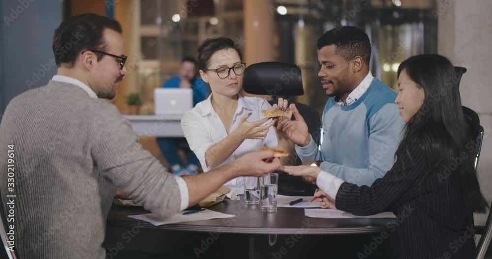 Happy multicultural workers having fun eating pizza at lunch Happy multicultural workers having fun eating pizza at lunch