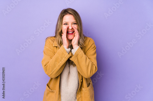 Young caucasian woman isolated on purple background saying a gossip, pointing to side reporting something.