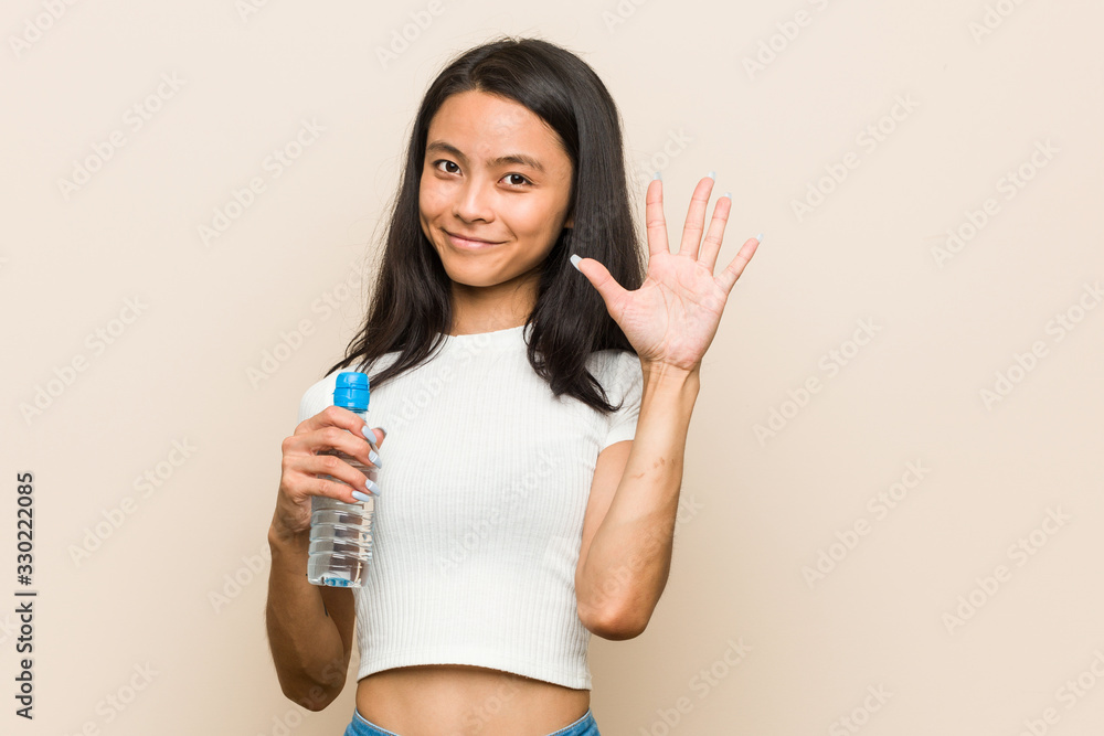 Young asian woman holding a water bottle smiling cheerful showing number five with fingers. Young asian woman holding a water bottle smiling cheerful showing number five with fingers.